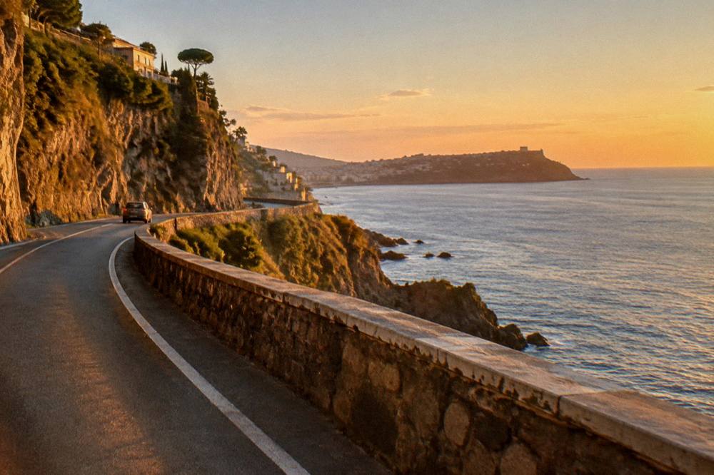 Coastal road winding along cliffs above the sea toward a distant headland