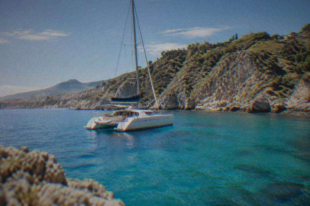 Catamaran anchored in a clear turquoise bay with rocky cliffs behind