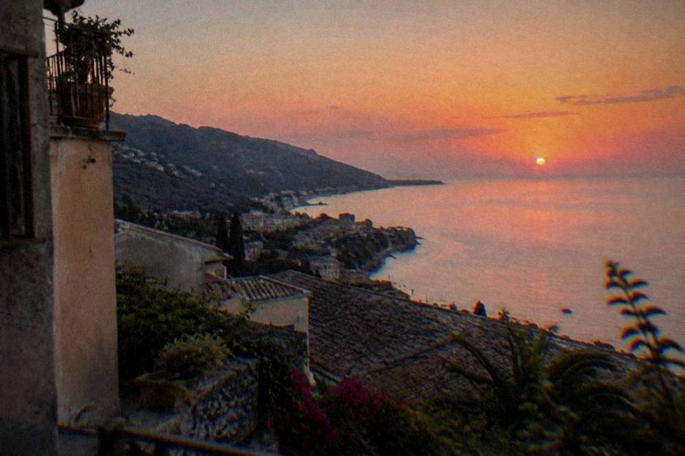 Coastal town on a cliff terrace with rooftops and sea horizon at sunset