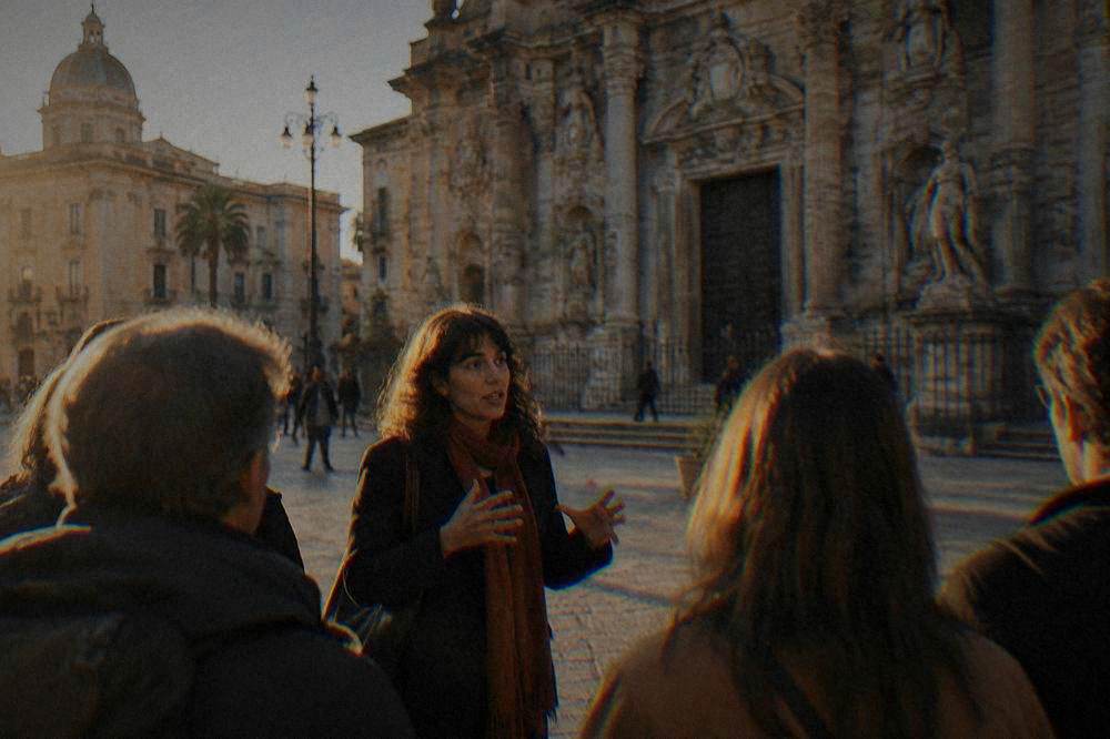A guide speaking to a small group of visitors in a Palermo square near a ornate church facade