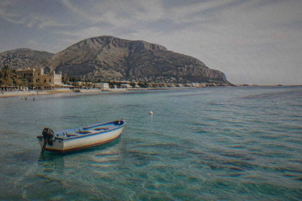 A small boat on clear turquoise water along the coast near Palermo