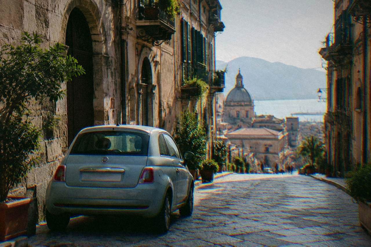 A rental car parked on a narrow sunlit street in the historic centre of Palermo
