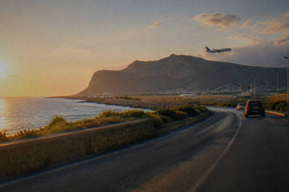 A coastal road curving along the Sicilian coast with hills in the distance