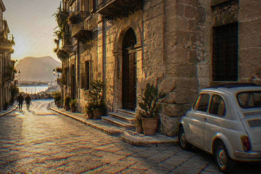 A stone building at the edge of a narrow Palermo street with a small car parked outside