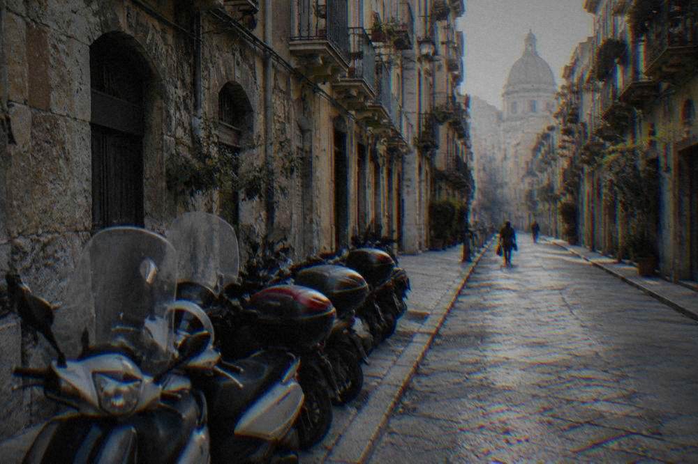 Scooters parked tightly along the kerb of a narrow street lined with old buildings in Palermo