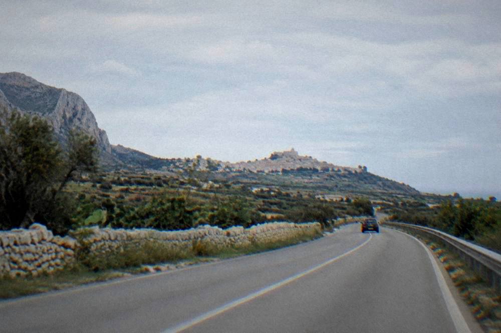 An open road through the Sicilian countryside with a distant hilltop town
