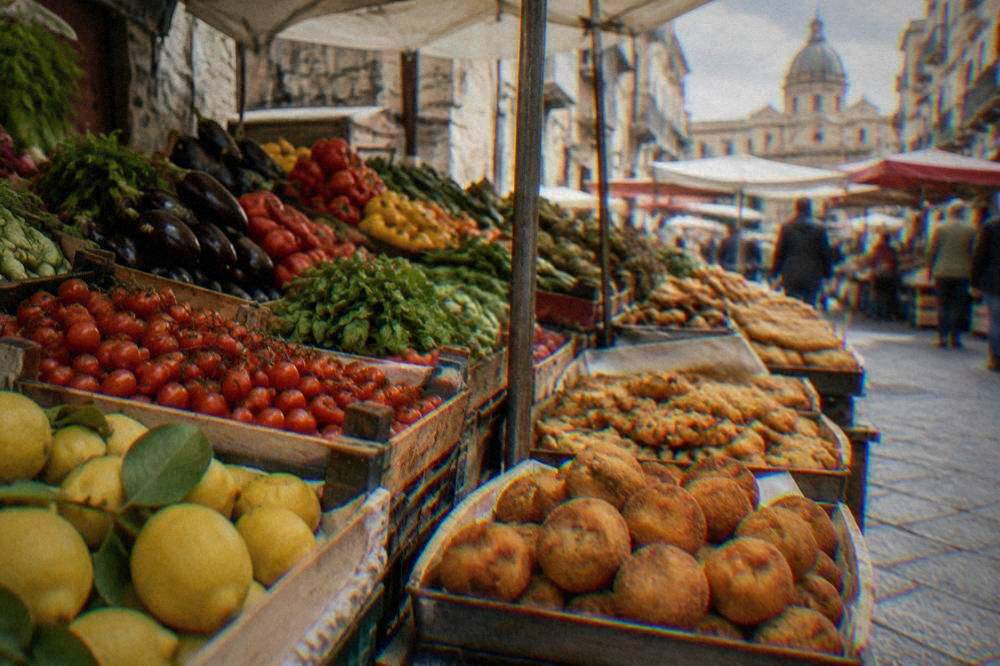 A street market stall in Palermo piled with fresh produce and fried snacks