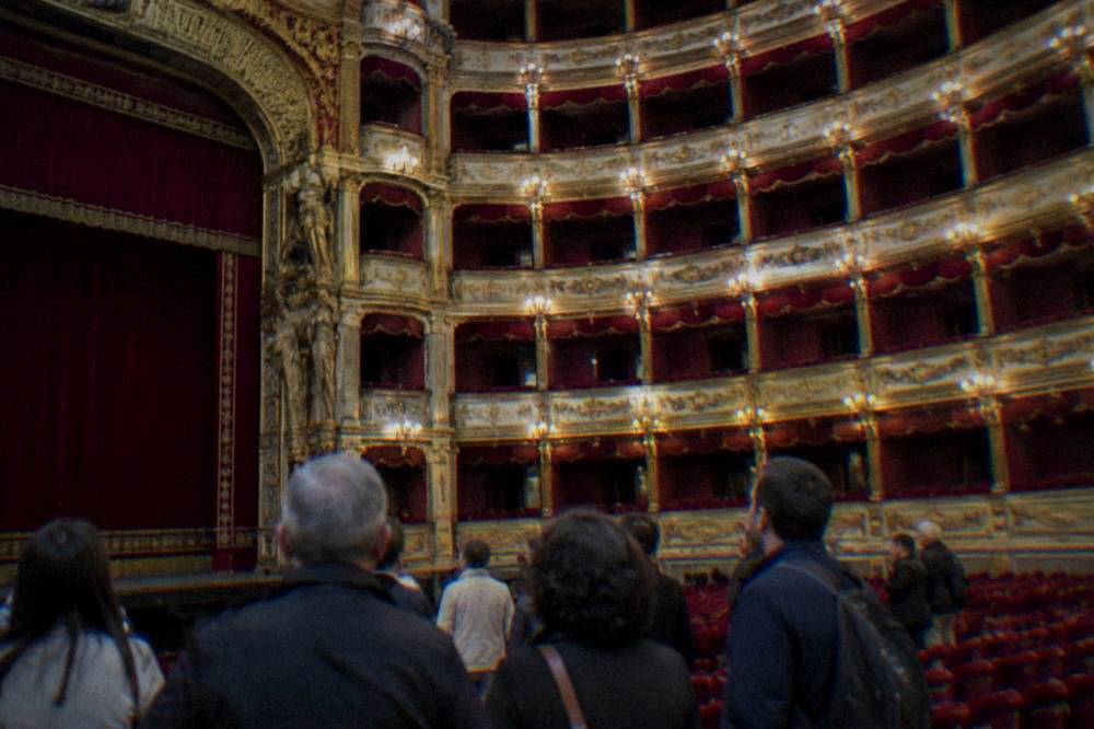 A guided tour group standing inside the richly decorated auditorium of the Teatro Massimo
