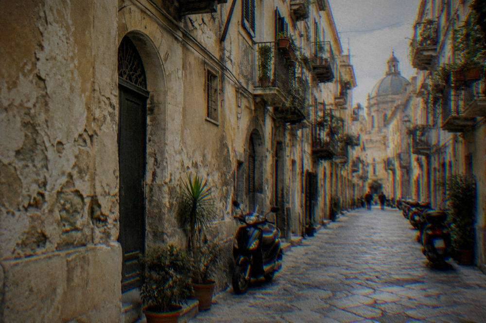 A narrow old street in central Palermo with weathered facades and scooters parked along the wall