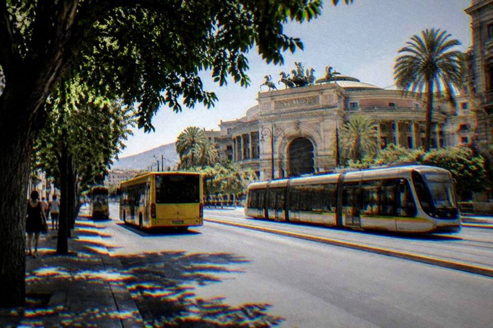 A yellow AMAT bus and a tram passing on a central Palermo street near the Politeama theatre