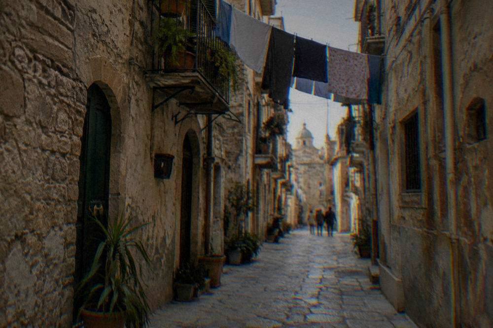 A narrow old-town street in Palermo with worn stone buildings and laundry overhead