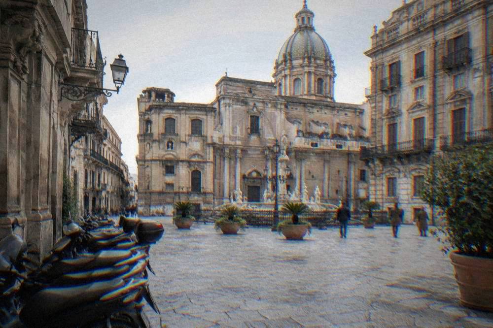 A sunny square in the old centre of Palermo with baroque facades and parked scooters