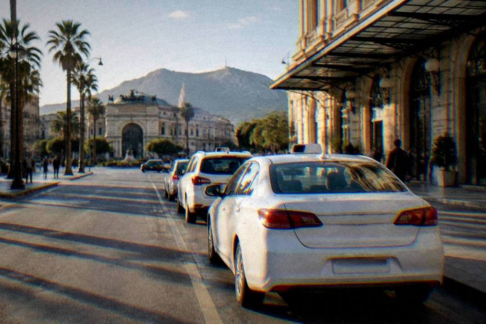 A white licensed taxi waiting at a rank outside a station in Palermo