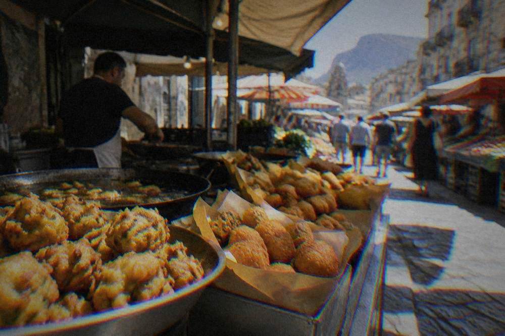 A street food stall under an awning with a counter of golden fried snacks in paper