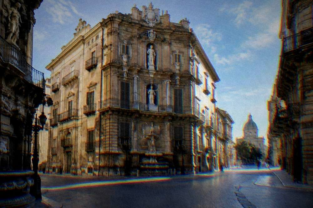A curved Baroque limestone facade with a fountain at an empty crossroads in early morning