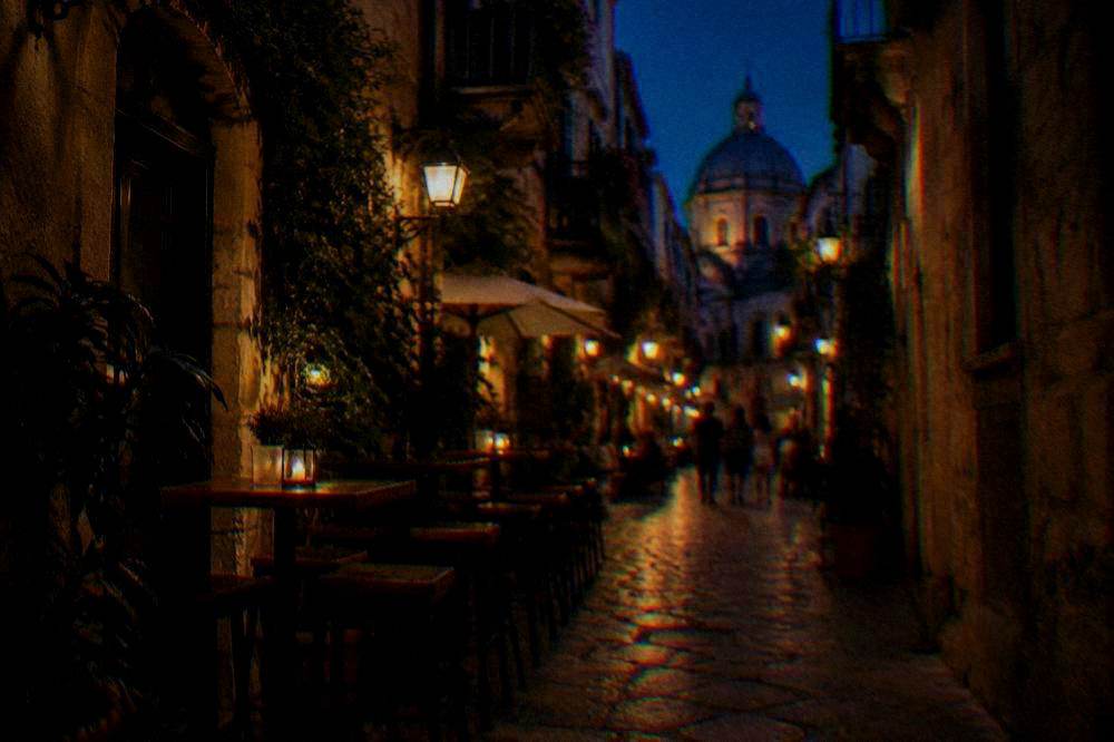A narrow old-town lane at night lit by warm lanterns with outdoor bar tables