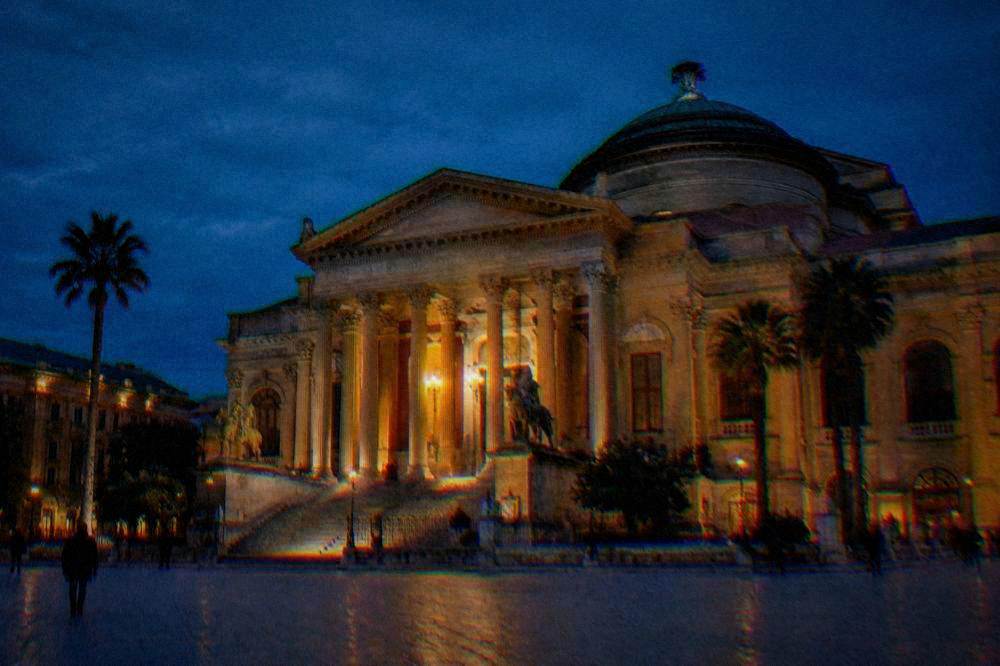 A floodlit neoclassical opera house with a green dome at blue hour
