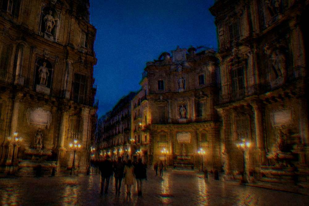A small group walking through a floodlit Baroque crossroads at blue hour