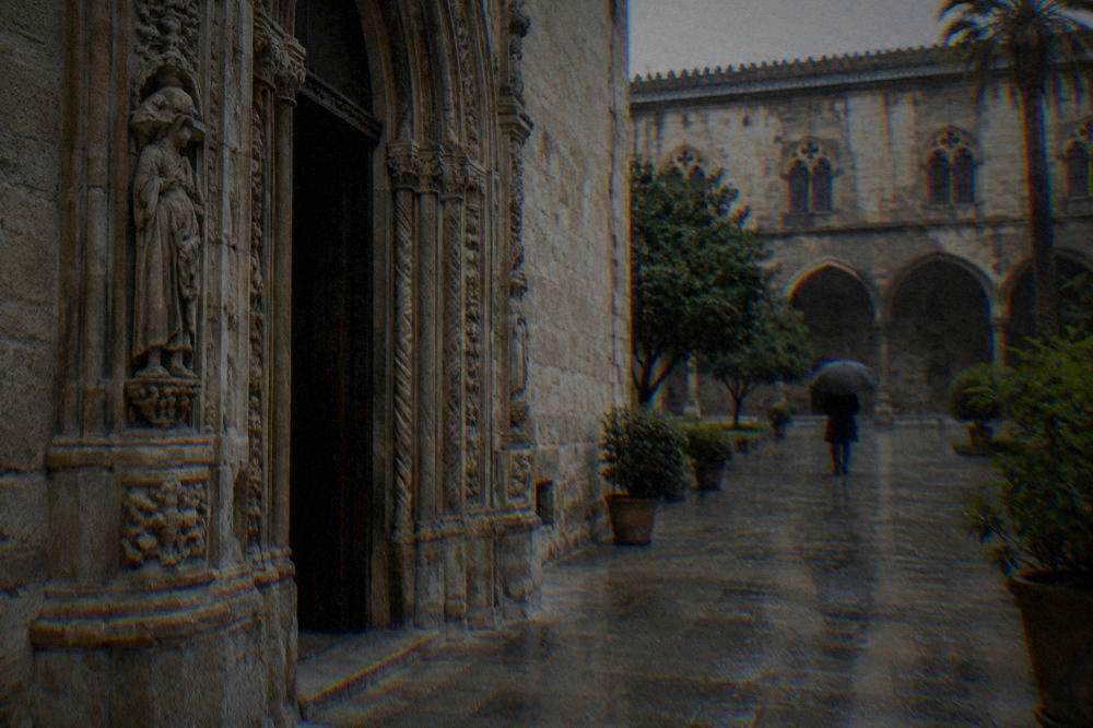 A late-Gothic palace portal and courtyard with wet paving on a rainy day