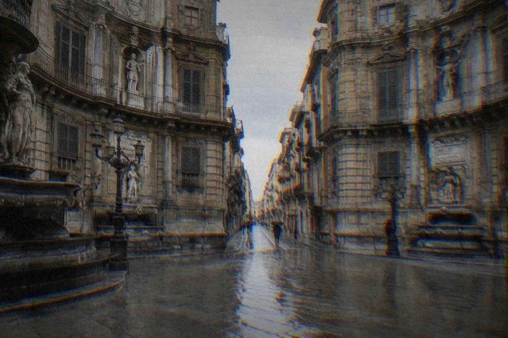 A wet Baroque crossroads of curved limestone facades with reflections on the paving on a rainy day