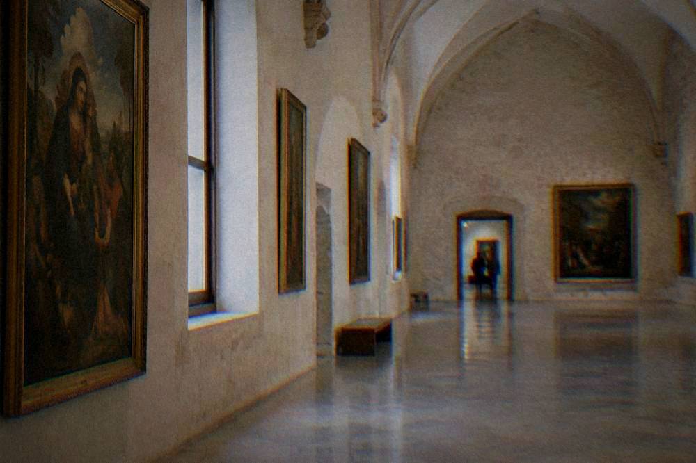 A bright museum gallery hall with a vaulted ceiling, old paintings on pale walls and a polished floor