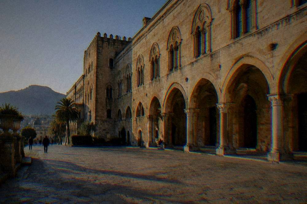 A long golden-stone palace facade with arches in low winter sun above a quiet forecourt