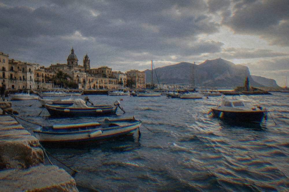 Moored boats at a small old harbour under heavy cloud with choppy grey-blue water