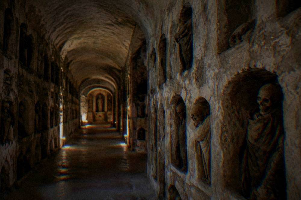 A long vaulted underground stone corridor with arched niches in dim warm light