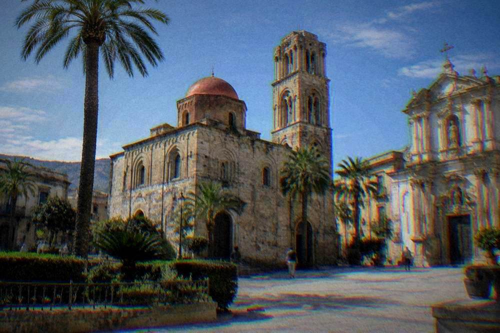 A small Norman church with a red dome and a Romanesque bell tower beside a Baroque facade