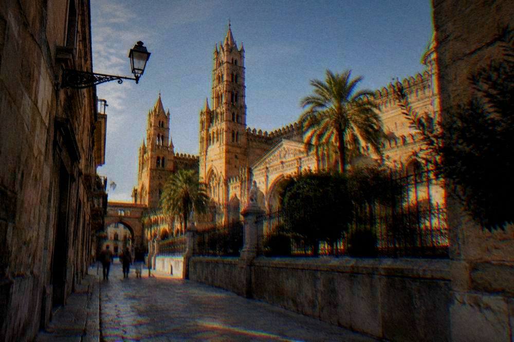 A large golden-limestone cathedral with battlemented towers and pointed arches seen from a quiet side street
