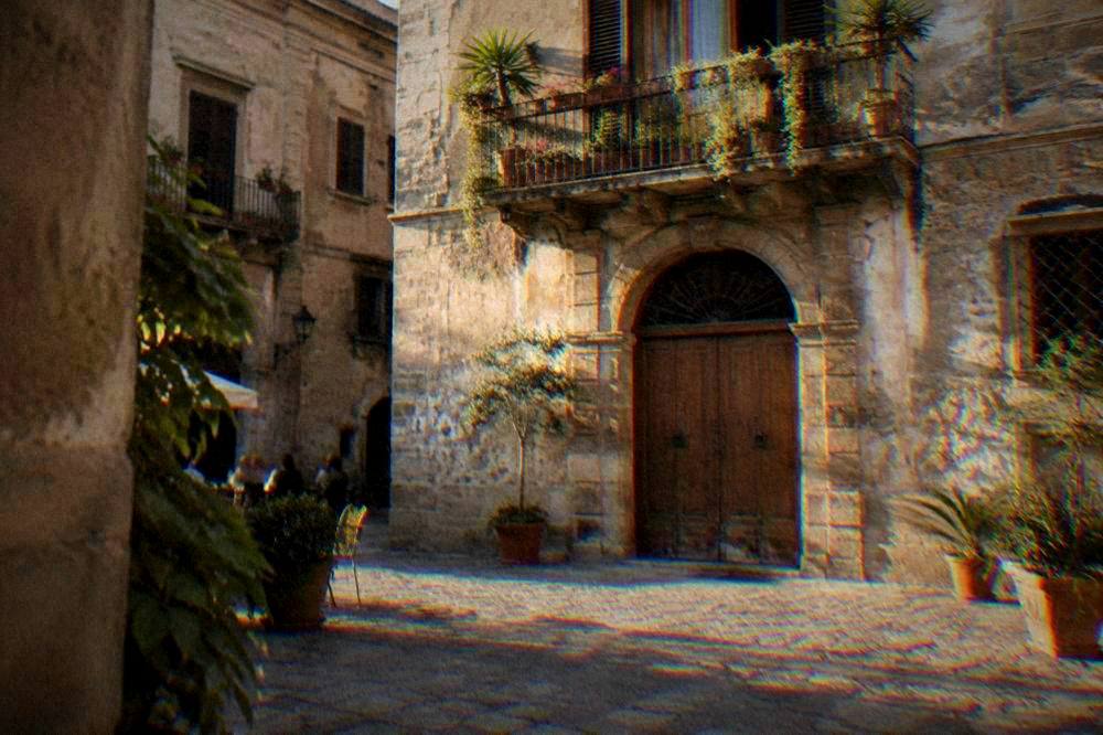 A small palazzo courtyard with an old wooden door and a balcony with potted plants