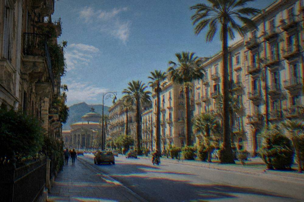 A residential boulevard of tall apartment buildings with iron balconies and palm trees