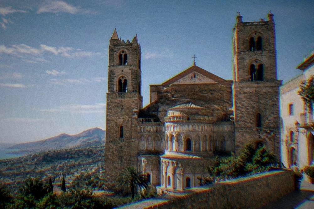 A large Norman cathedral between two towers with a tiered apse above a green valley