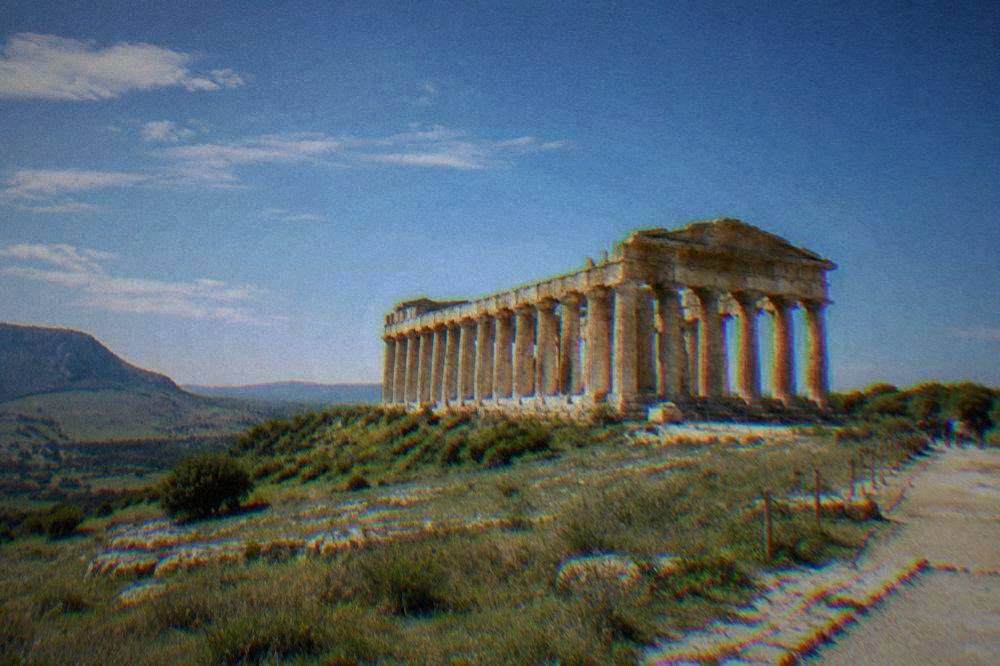 A tawny Doric temple of tall columns standing alone on a green hillside under a wide sky
