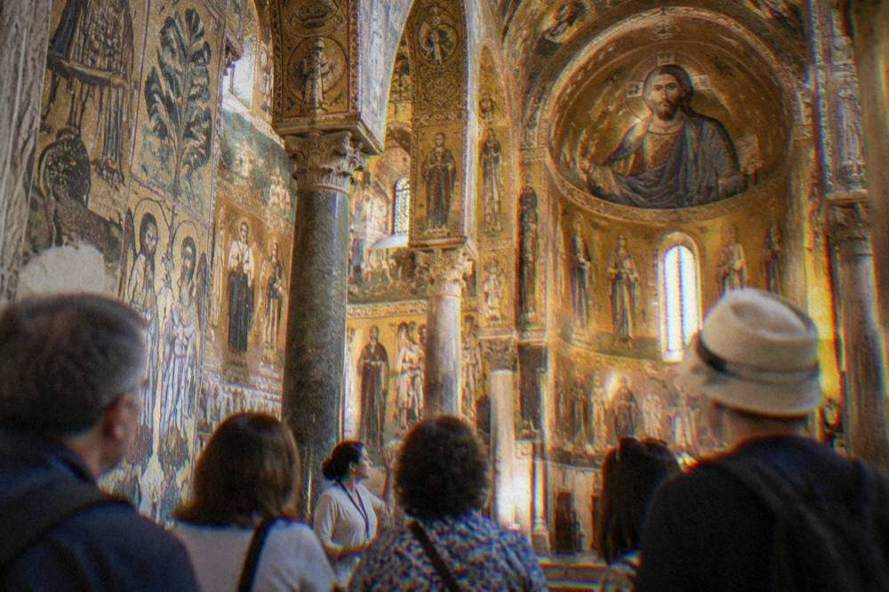 A guided group listening to a guide inside a gilded mosaic chapel in Palermo