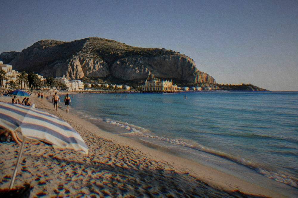 A seaside town with a sandy beach and a rocky headland under a clear sky