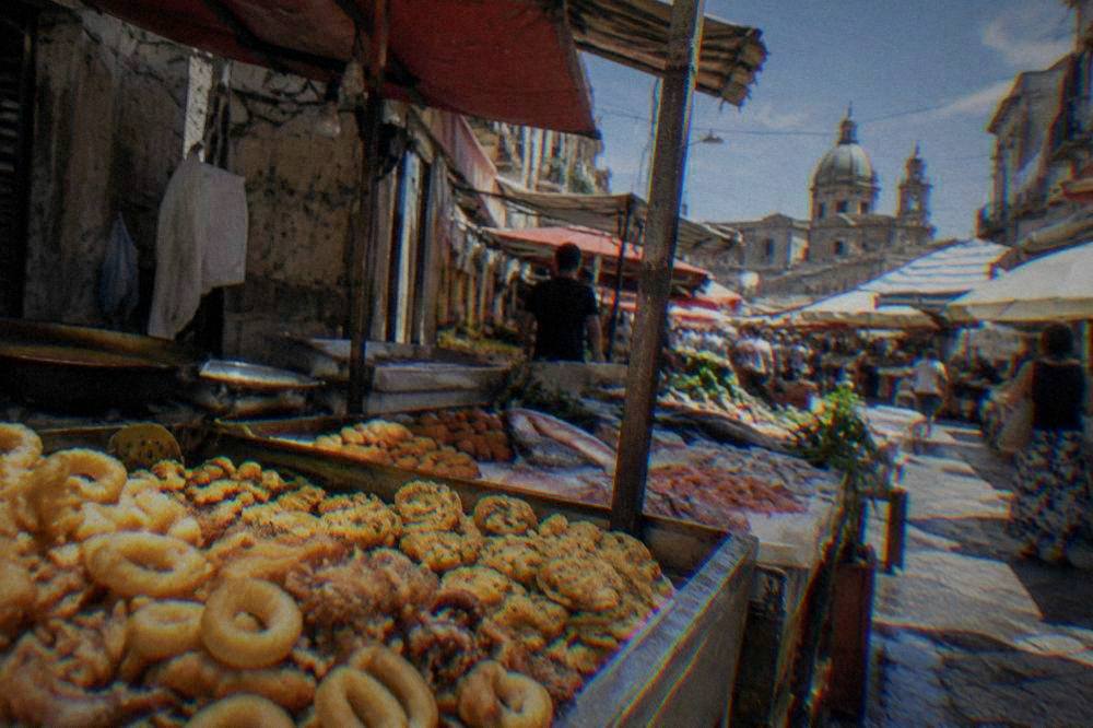 A busy Palermo street market stall with fried snacks and trays of seafood