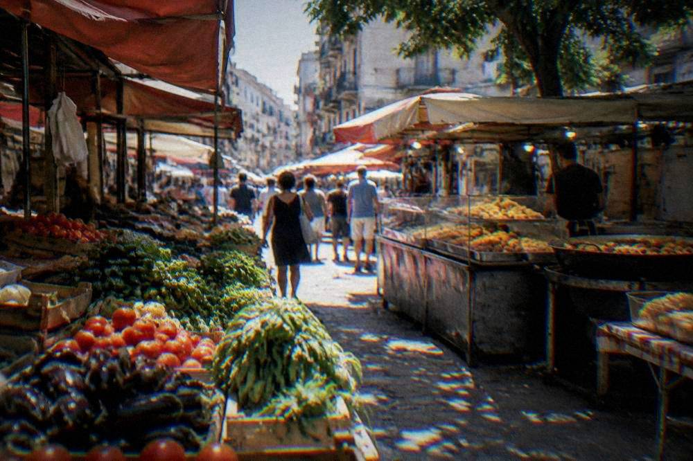 Stalls of vegetables and fried street food in a busy Palermo market alley