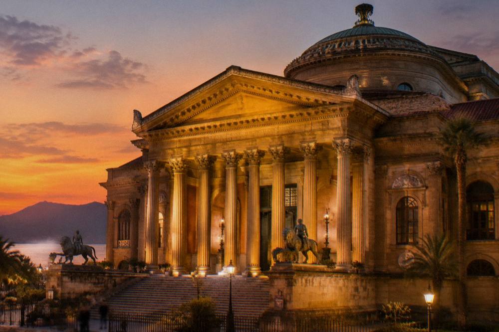 The illuminated facade of the Teatro Massimo opera house at dusk