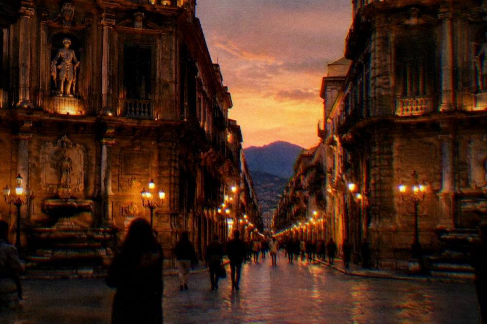 People strolling along Via Maqueda in the evening under lit buildings in Palermo