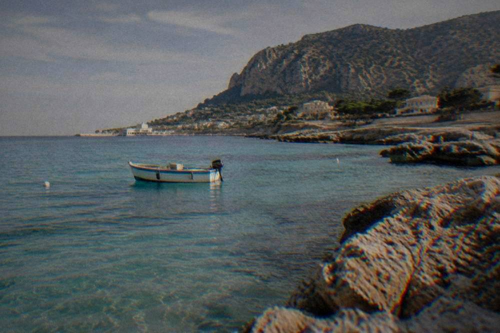 Small boat anchored in turquoise water near a rocky Sicilian coastline
