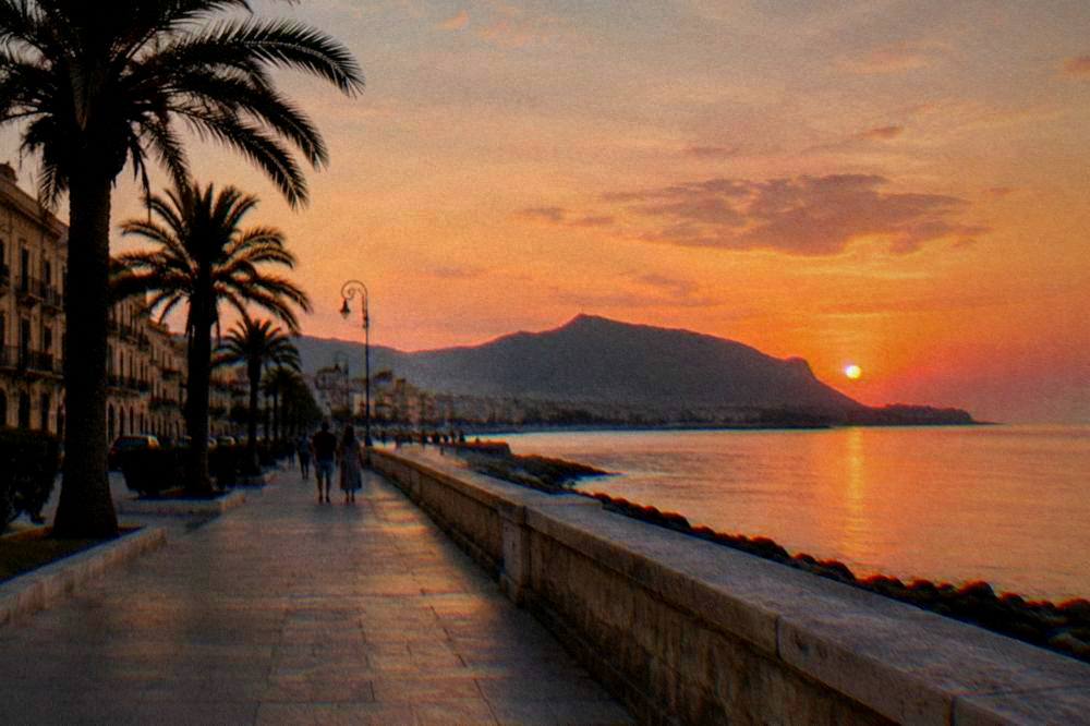 Evening light on a seafront promenade with palm trees and old buildings