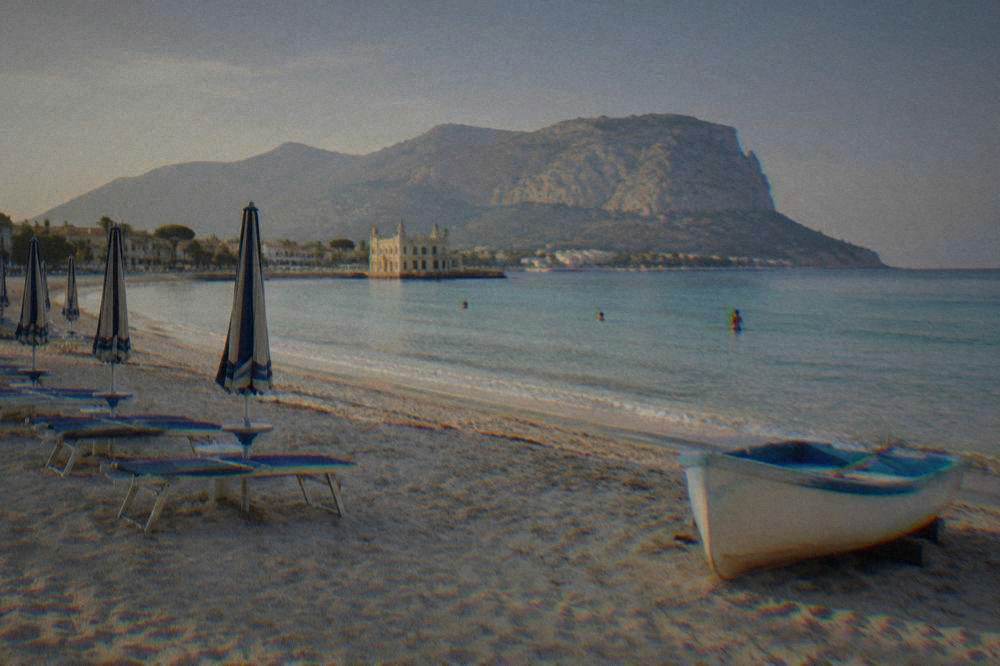 A wide sandy beach with shallow turquoise water, sunbeds and a parked small boat at Mondello