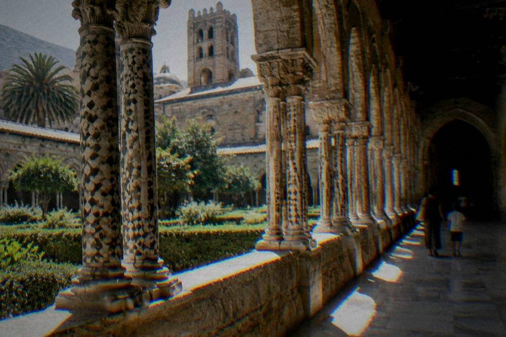 A cloister with paired columns and inlaid stone decoration at Monreale, a parent and child walking through