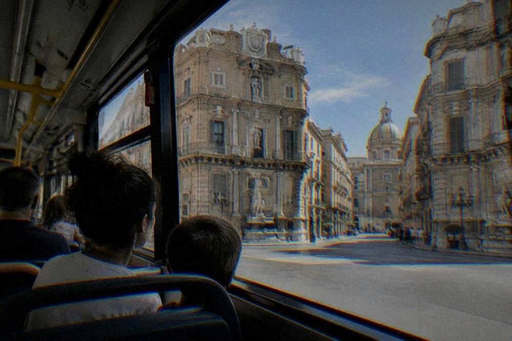 Parents and children riding a city bus past ornate buildings in central Palermo