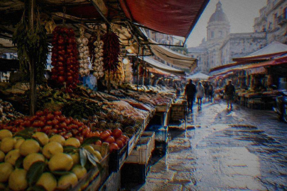 Covered food market stalls in Palermo with hanging produce and a wet street outside