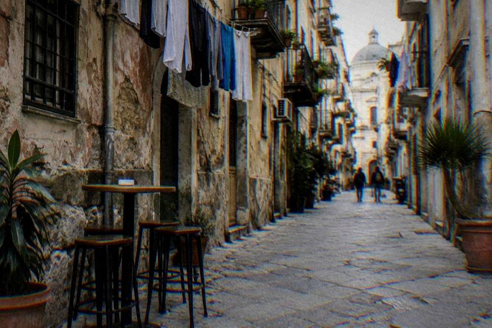 A Palermo side street with aged facades, laundry and a bar table set outside
