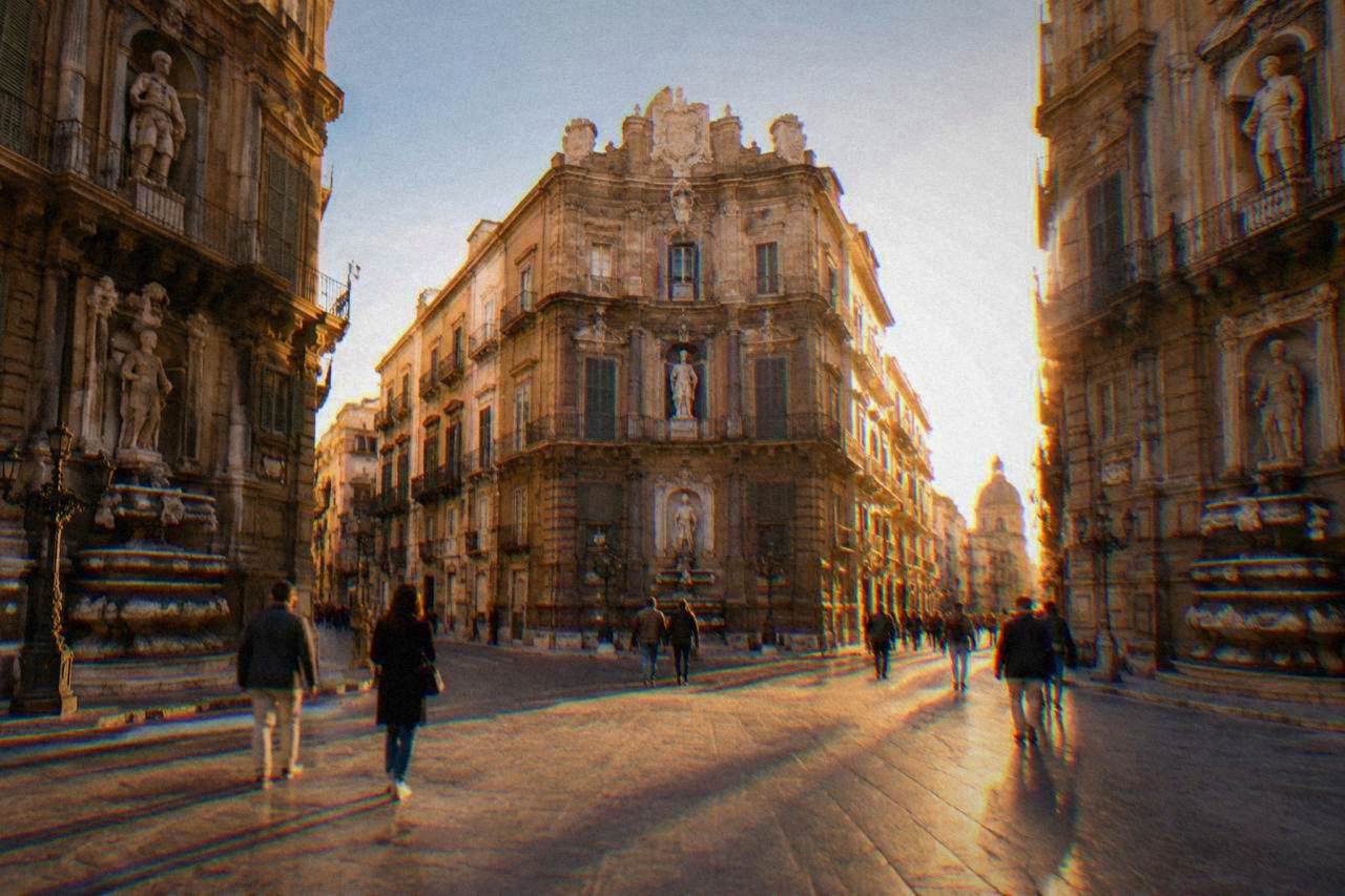 The four intersecting facades of the Quattro Canti square in Palermo at golden hour with pedestrians crossing