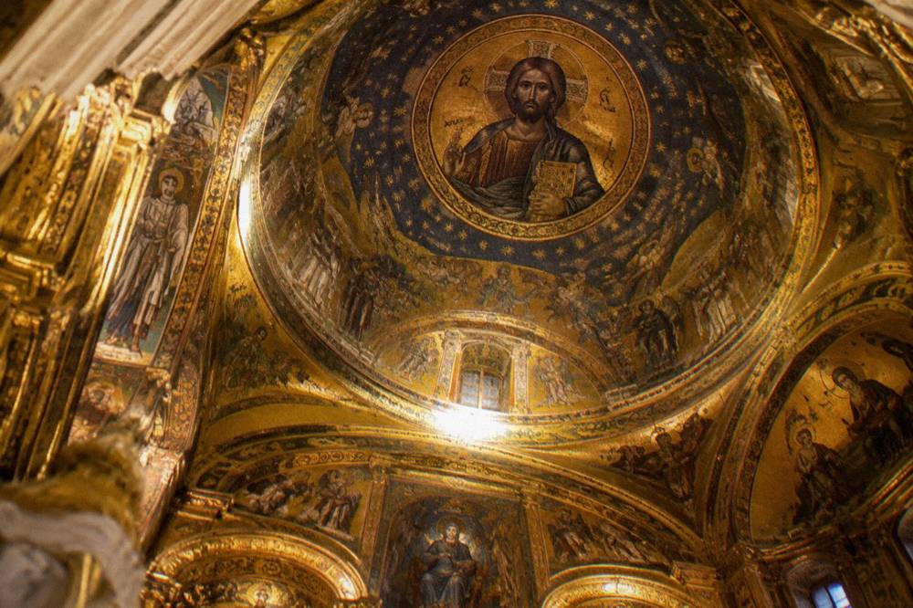 The mosaic ceiling and gilded interior of a chapel seen from below with warm reflected light
