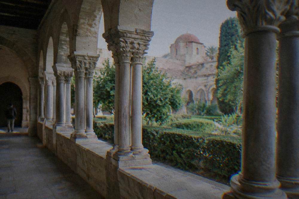 A cloister walkway with paired columns and a garden courtyard under a clear sky